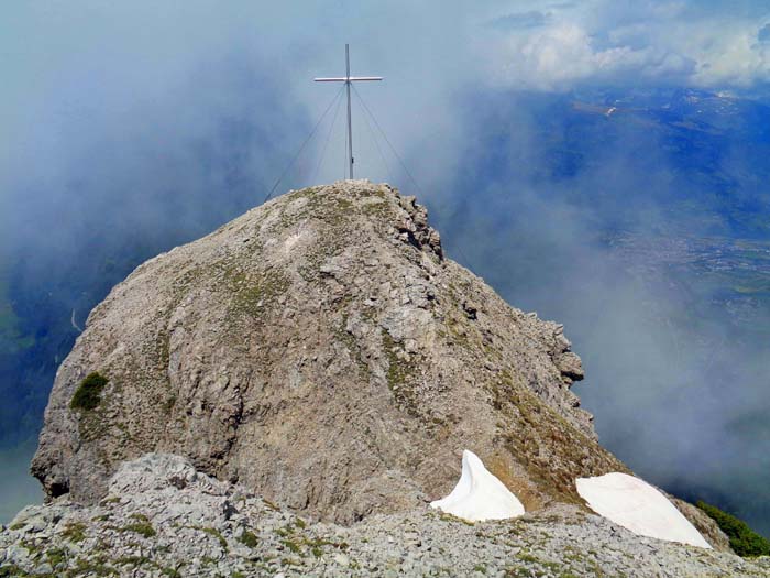 das Gipfelkreuz mit Buch steht auf einem felsigen Buckel nördlich des höchsten Punktes
