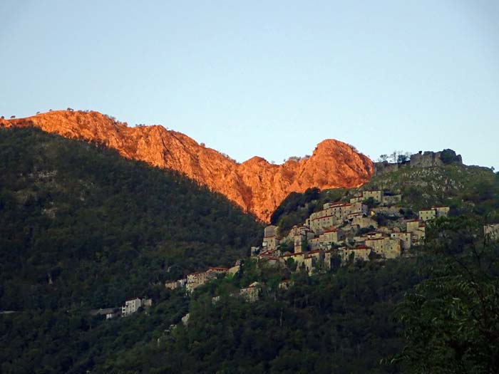 das Bergdorf Lúcchio klebt malerisch an den Steilhängen über der Limaschlucht; im Licht der aufgehenden Sonne links die Penna, rechts der kleine Buckel des schwierigeren Monte Memoriante
